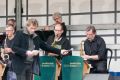 Drei Männer spielen Saxophon und der Dirigent hält ein Mikrofon davor