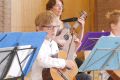 Ein Junge spielt Gitarre mit seiner Lehrerin im Hintergrund